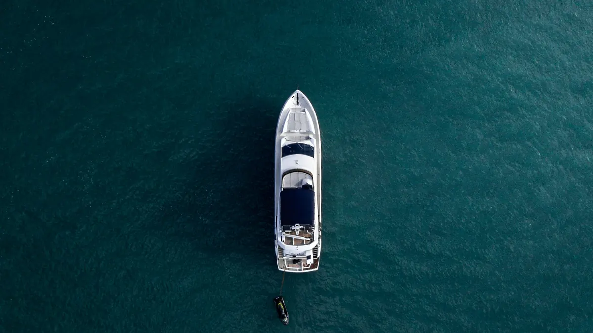 A white yacht crossing deep blue-green water, seen from directly above